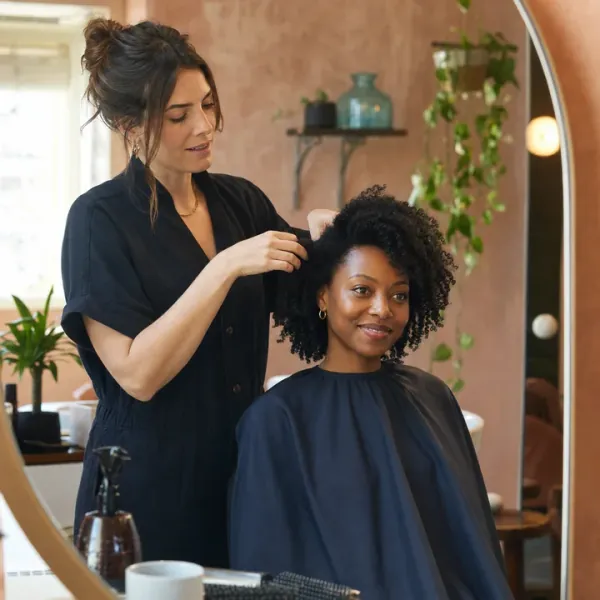 A stylist arranging a seated client's hair in front of a salon mirror